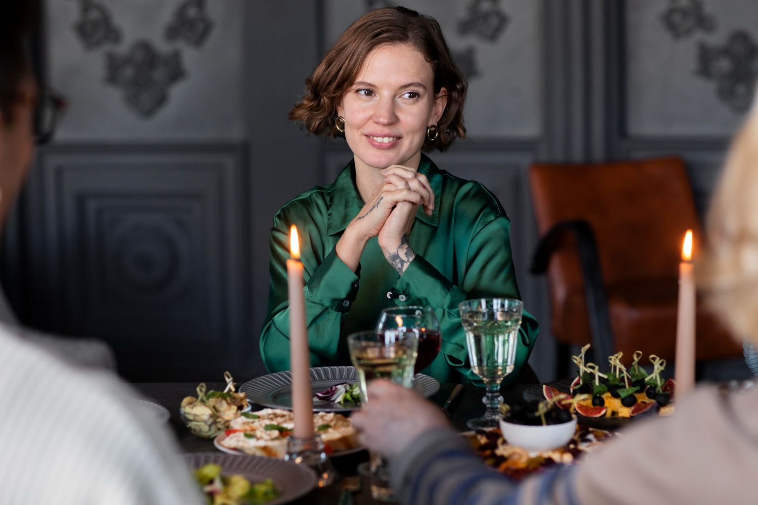 Mulher de camisa verde sorrindo à mesa de jantar com velas e convidados – a arte de receber com sofisticação