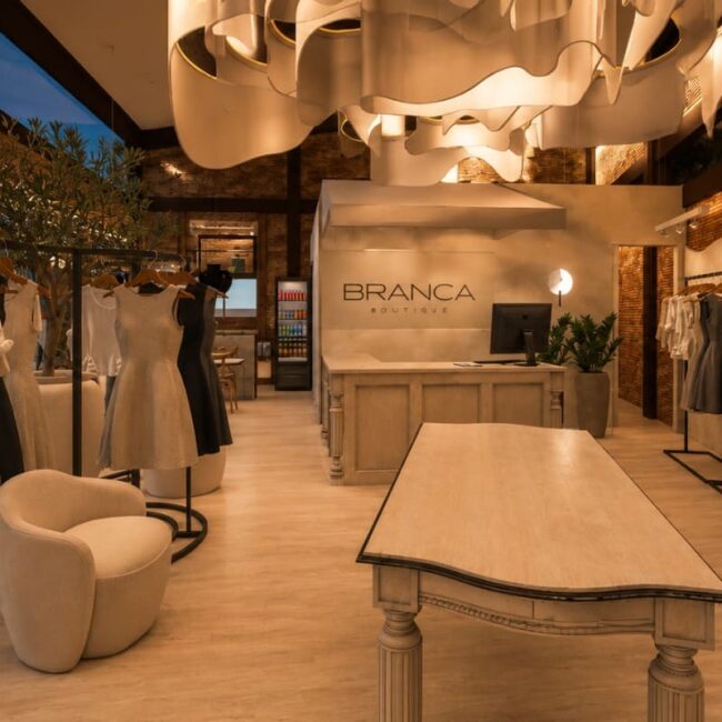 Interior projeto loja Branca Boutique Itaipava Petrópolis decoração teto orgânico araras roupas mesa central ambiente luxuoso