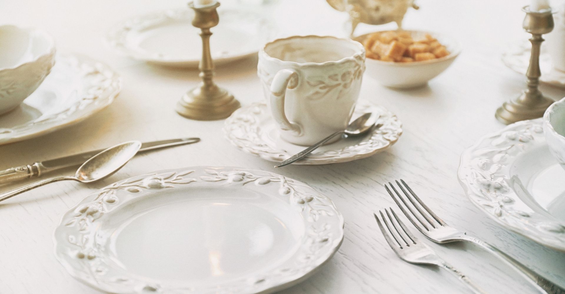 Talheres elegantes e louças de porcelana branca sobre mesa com castiçais de bronze – arte de receber com requinte